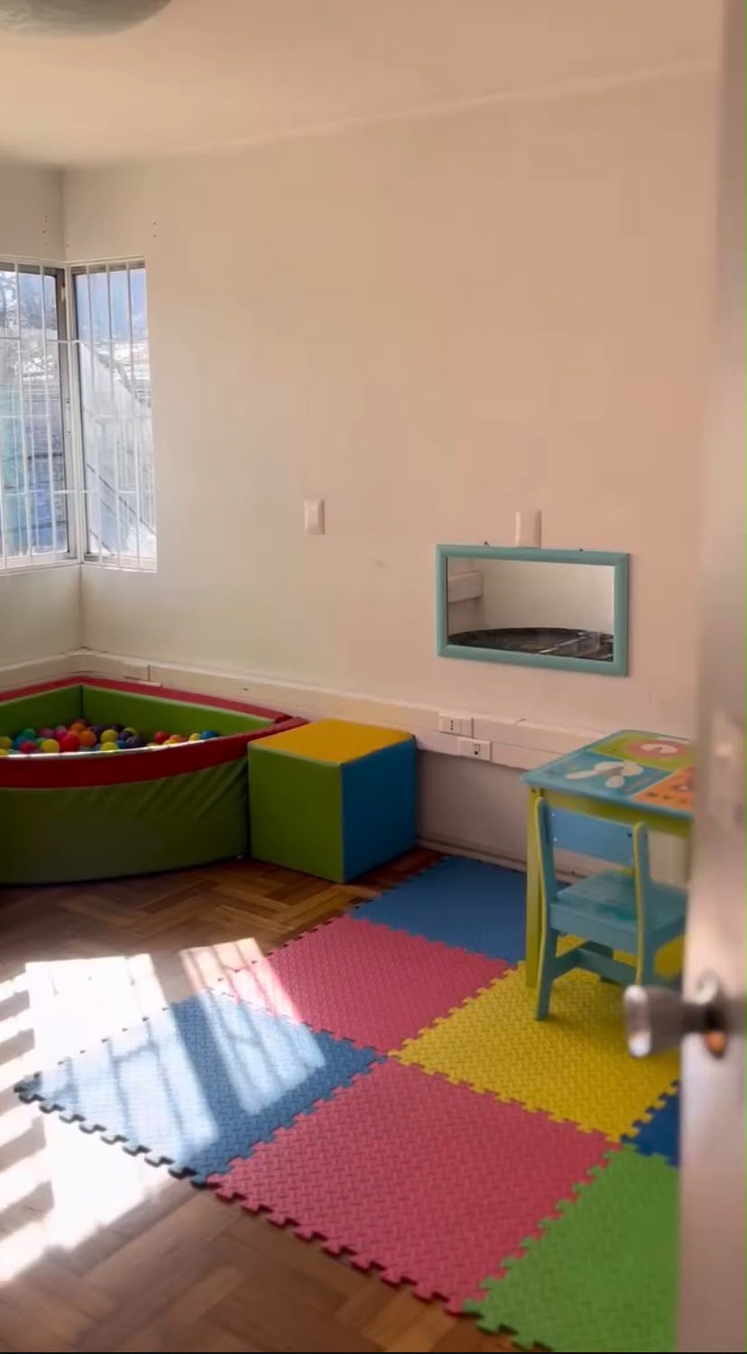 Sala de atención con pisos de colores, mesa infantil y piscina de pelotas